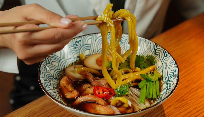 Reference image of a person lifting noodles from a bowl with chopsticks